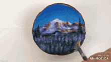 a person is painting a mountain scene on a wooden slice