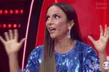 a woman in a blue sequined dress is sitting in front of a microphone with her hands up .