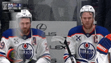 two hockey players wearing oilers uniforms sit in the stands