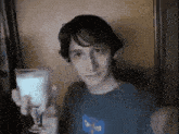a young man in a blue shirt is holding up a glass of milk