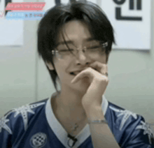 a young man wearing glasses and a blue shirt is laughing with his hand to his mouth .