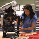 a woman in a blue shirt is working on a robot with a screwdriver that says ' t ' on it