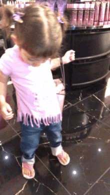 a little girl in a pink shirt and jeans stands in front of a display of cosmetics