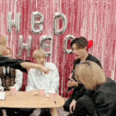 a group of people are sitting around a table with balloons that say hbd