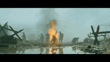 a group of soldiers standing around a fire in a muddy field
