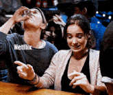 a man is drinking from a shot glass and a woman is laughing while watching netflix .