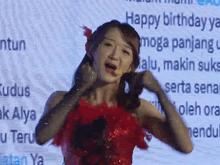 a woman in a red dress stands in front of a screen that says " happy birthday "
