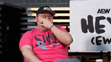 a man wearing a pink shirt with the word sins on it covering his face