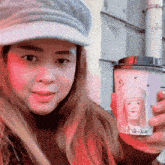 a woman wearing a hat is holding a cup of coffee with a picture of a girl on it