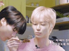 a man with pink hair is eating food from another man 's hand .