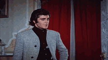 a man standing in front of a red curtain wearing a grey jacket