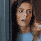 a woman in a blue shirt is looking out a window
