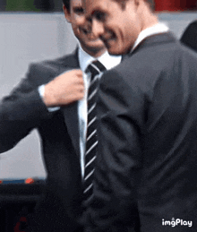 two men in suits and ties are standing next to each other and one is adjusting his tie