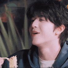 a young man in a blue hoodie is eating noodles with a fork