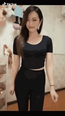 a woman in a black crop top and black pants is standing in front of a stuffed animal shelf .