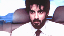 a man with a beard wearing a white shirt and tie is sitting in the back seat of a car