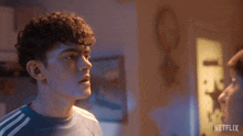 a young man with curly hair is standing in a dark room with a netflix logo in the corner .