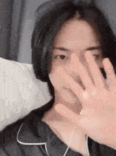 a young man is covering his face with his hand while laying in bed .