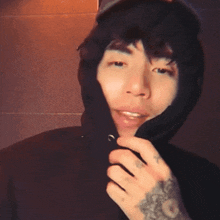 a man with a tattoo on his arm is wearing a black hooded jacket