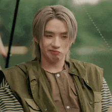 a young man wearing a striped shirt and a green vest making a funny face