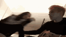 a man with red hair is playing an ukulele while a woman holds his hand .