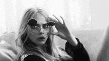 a black and white photo of a woman wearing sunglasses and looking through them .