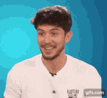 a man with a beard wearing a white t-shirt is smiling .