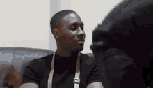 a man in a black shirt is sitting on a couch talking to someone .