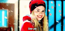 a woman wearing a red hat and a red jacket is smiling and saying see ya .