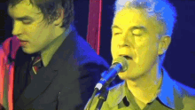 a man singing into a microphone while another man plays a guitar