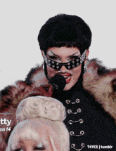 a woman in a fur coat is singing into a microphone while wearing sunglasses and a mask