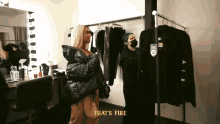 a woman in a black jacket is standing next to a man in a mask and a sign that says that 's fire on it