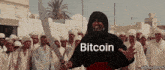a man is holding a sword in front of a crowd and the word bitcoin is on his shirt