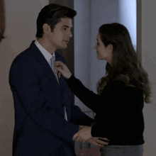 a man in a suit and tie is being helped by a woman in a black sweater