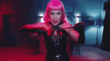 a woman in a pink wig and black gloves is holding a whip in her mouth .