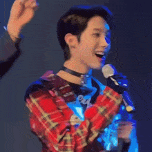 a man in a plaid shirt is singing into a microphone with his mouth open