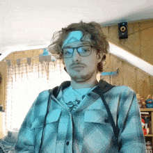 a man wearing glasses and a plaid shirt has a bandage on his forehead