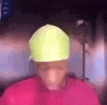 a man wearing a pink shirt and a yellow hat is looking at the camera .