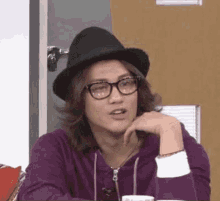 a young man wearing glasses and a hat is sitting at a table .