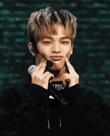 a young man is holding a microphone and smiling while wearing a black hoodie .