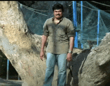a man wearing a watch is standing next to a large rock