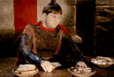 a man in armor sits at a table with a bowl of food