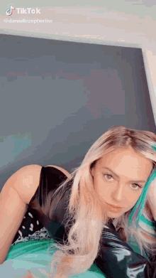 a woman with blonde hair and blue streaks is posing for a tiktok video .