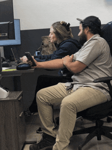 a man and a woman sit at a desk looking at a phone