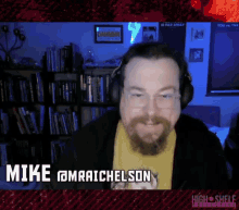 a man with a beard is wearing headphones and the name mike @mraichelson is on the screen