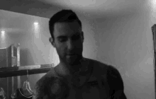 a black and white photo of a shirtless man with a tattoo on his chest