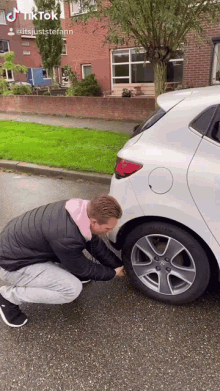 a man is changing a tire on a white car with tiktok written on the bottom right corner