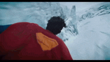a man in a red superman costume is walking through a snowy mountain .