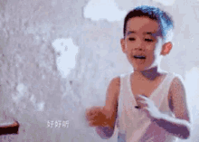 a little boy in a white tank top is standing in front of a white wall .