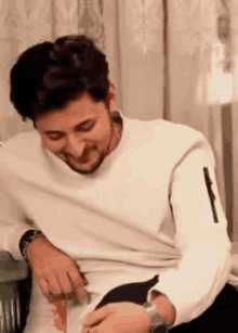 a man in a white sweater is laughing while holding a piece of paper .